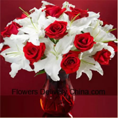 Rose rosse e gigli bianchi con alcune felci in un vaso di vetro