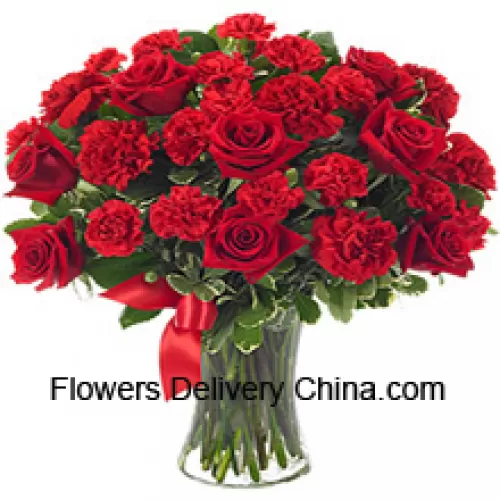12 rose rosse e 12 garofani rossi con alcune felci in un vaso di vetro